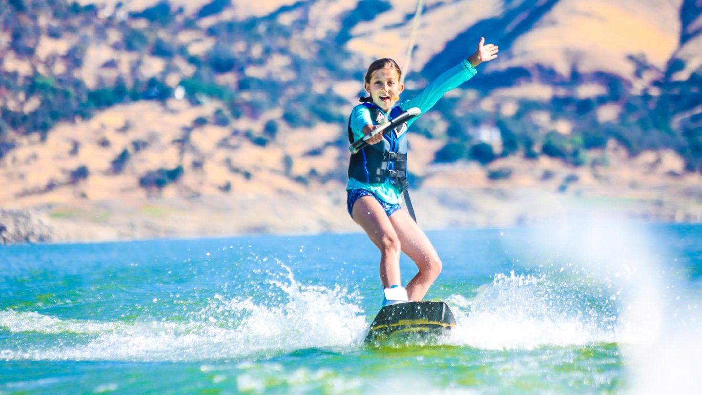A camper with her hand up in the air while wake boarding.