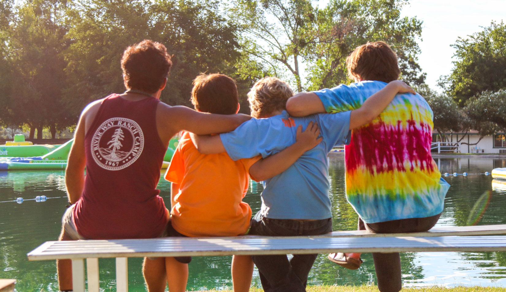 Campers sitting on a bench overlooking a lake with their arms around each other.
